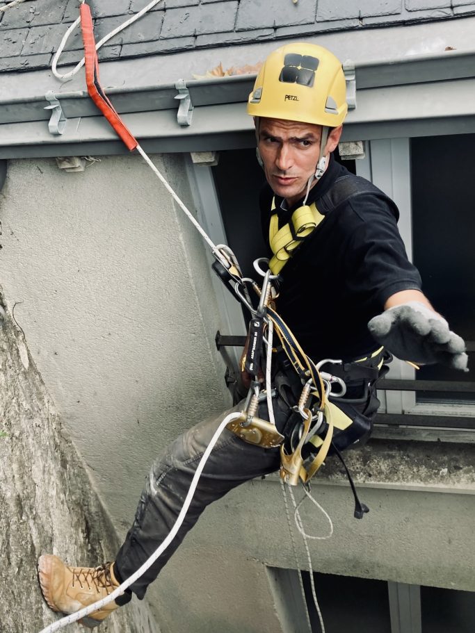 Intervention de couverture en accès difficile, techniques de travaux sur cordes Couvreur cordiste intervenant sur un bâtiment en accès difficile